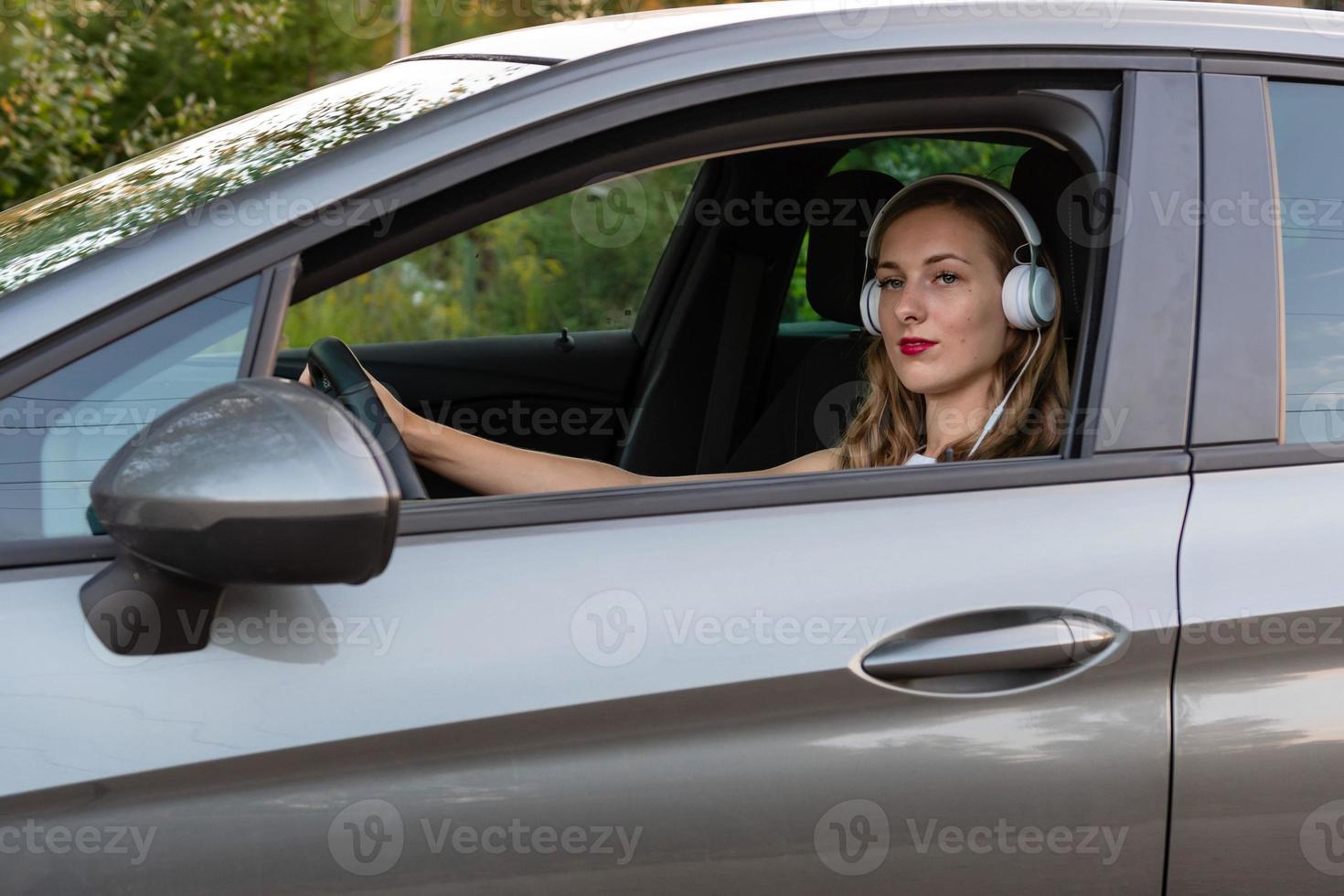 en ung, vacker kvinna med långt hår och hörlurar sitter vid ratten i bilen. foto