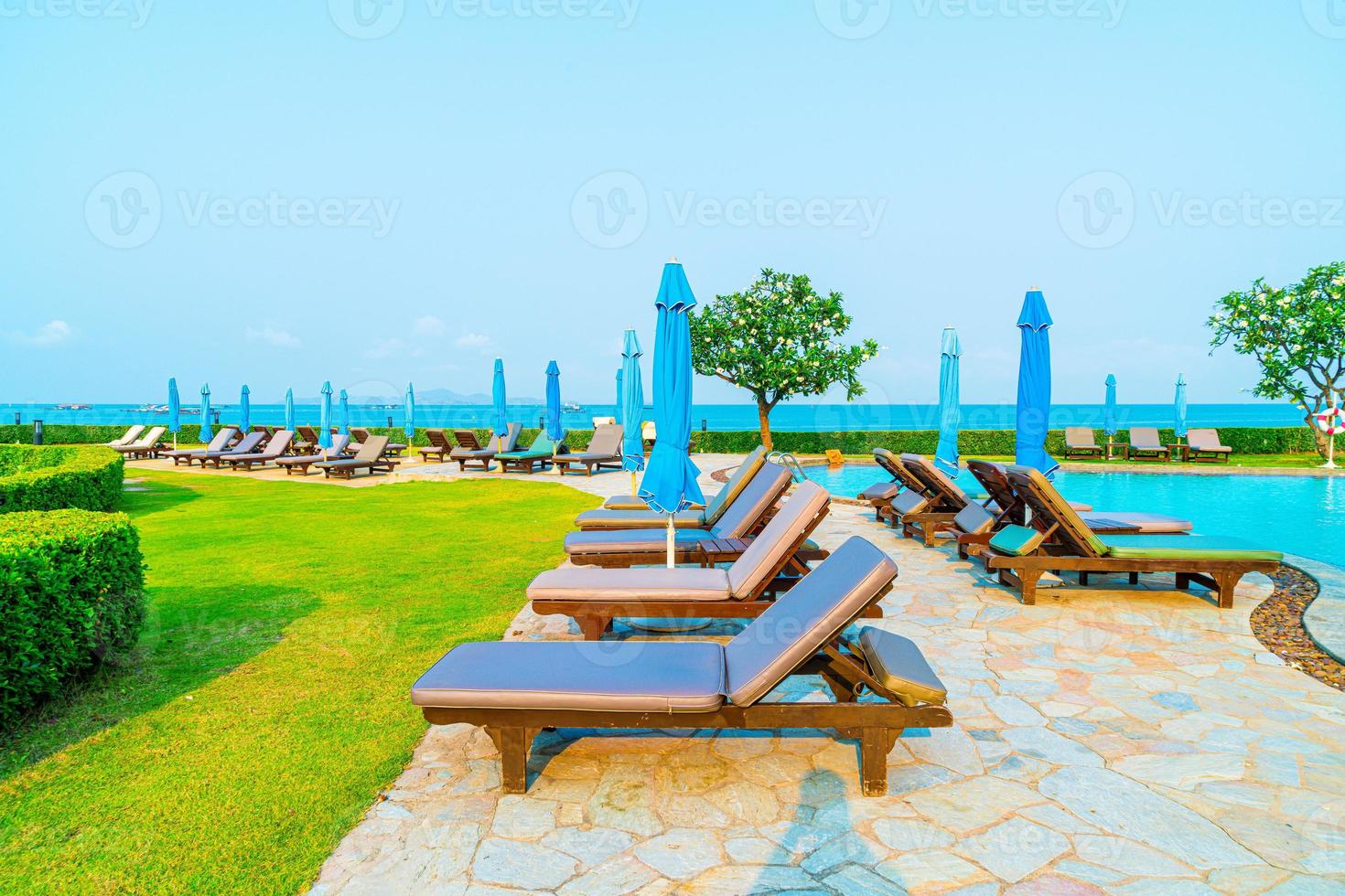 stolbassänger eller sängar och paraplyer runt poolen med havsbakgrund - semester och semesterkoncept foto