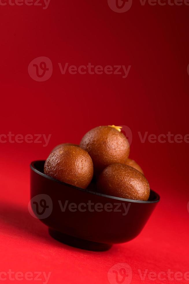 gulab jamun i svart skål på röd bakgrund. indisk efterrätt eller söt maträtt. foto