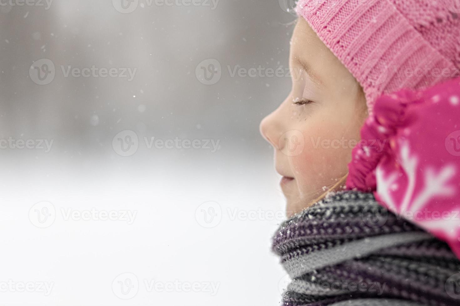 porträtt av en liten flicka i rosa närbild. ett barn njuter av snöfallet. jullov foto