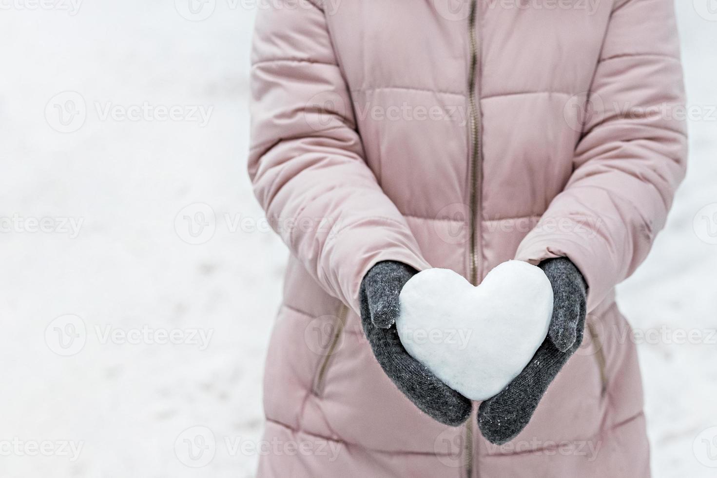 kvinnors händer i varma grå vantar med ett snövitt hjärta. begreppet alla hjärtans dag foto