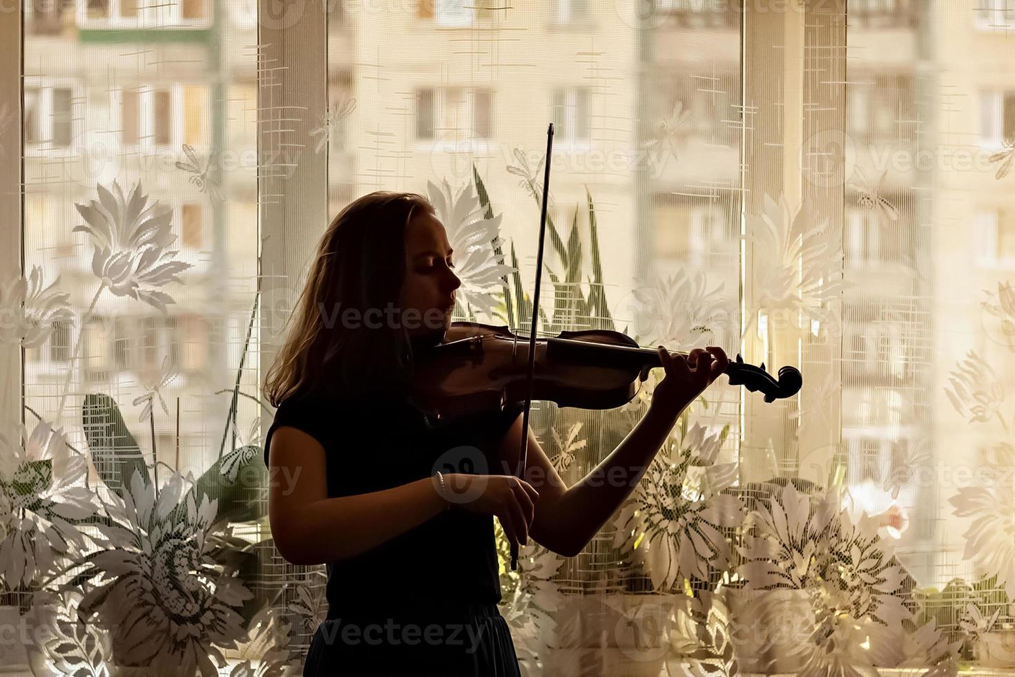 silhuett av en ung flicka, en musiker. spelar fiol i fönstrets bakgrund foto