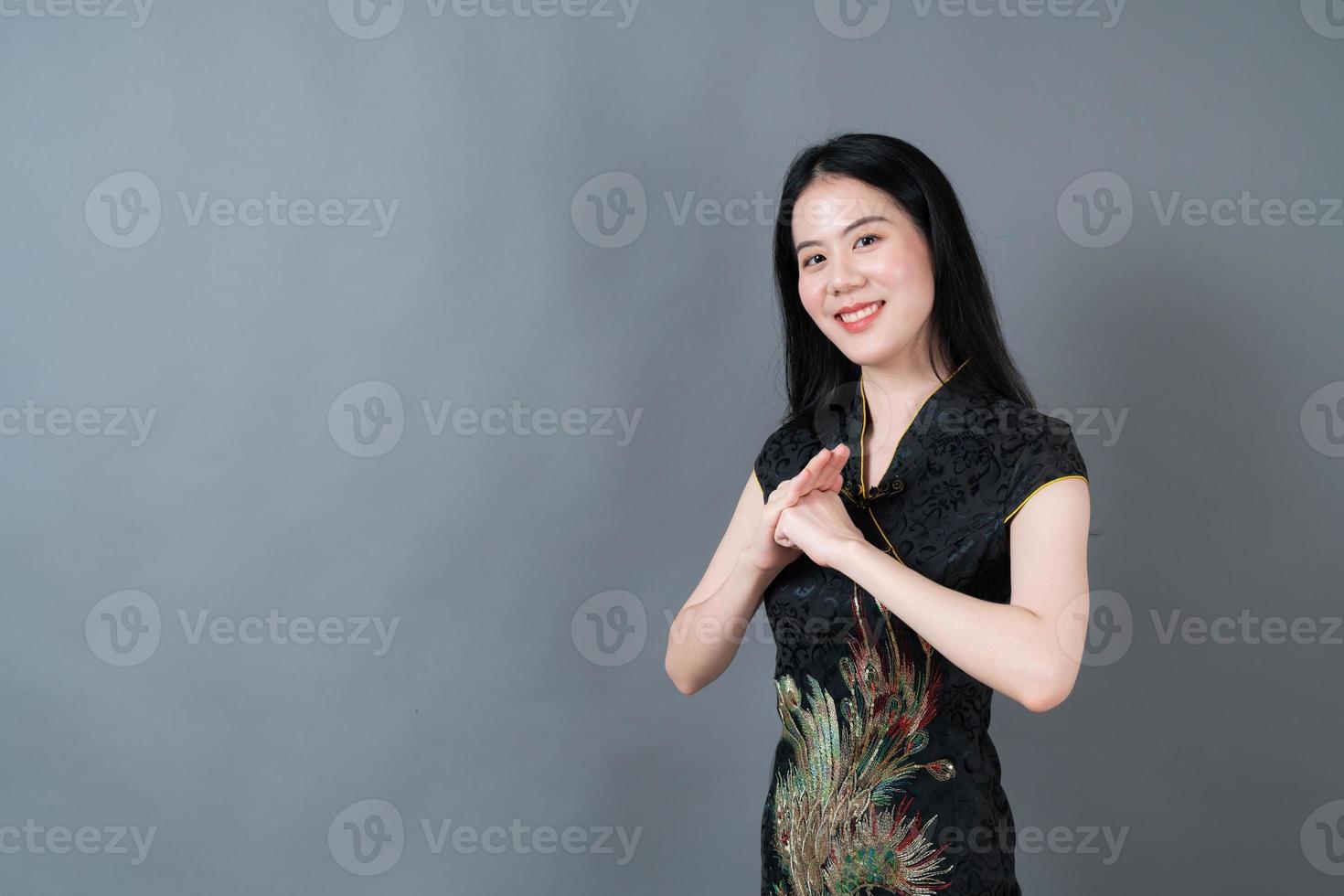 glad vacker ung asiatisk kvinna bär kinesisk traditionell klänning på grå bakgrund foto