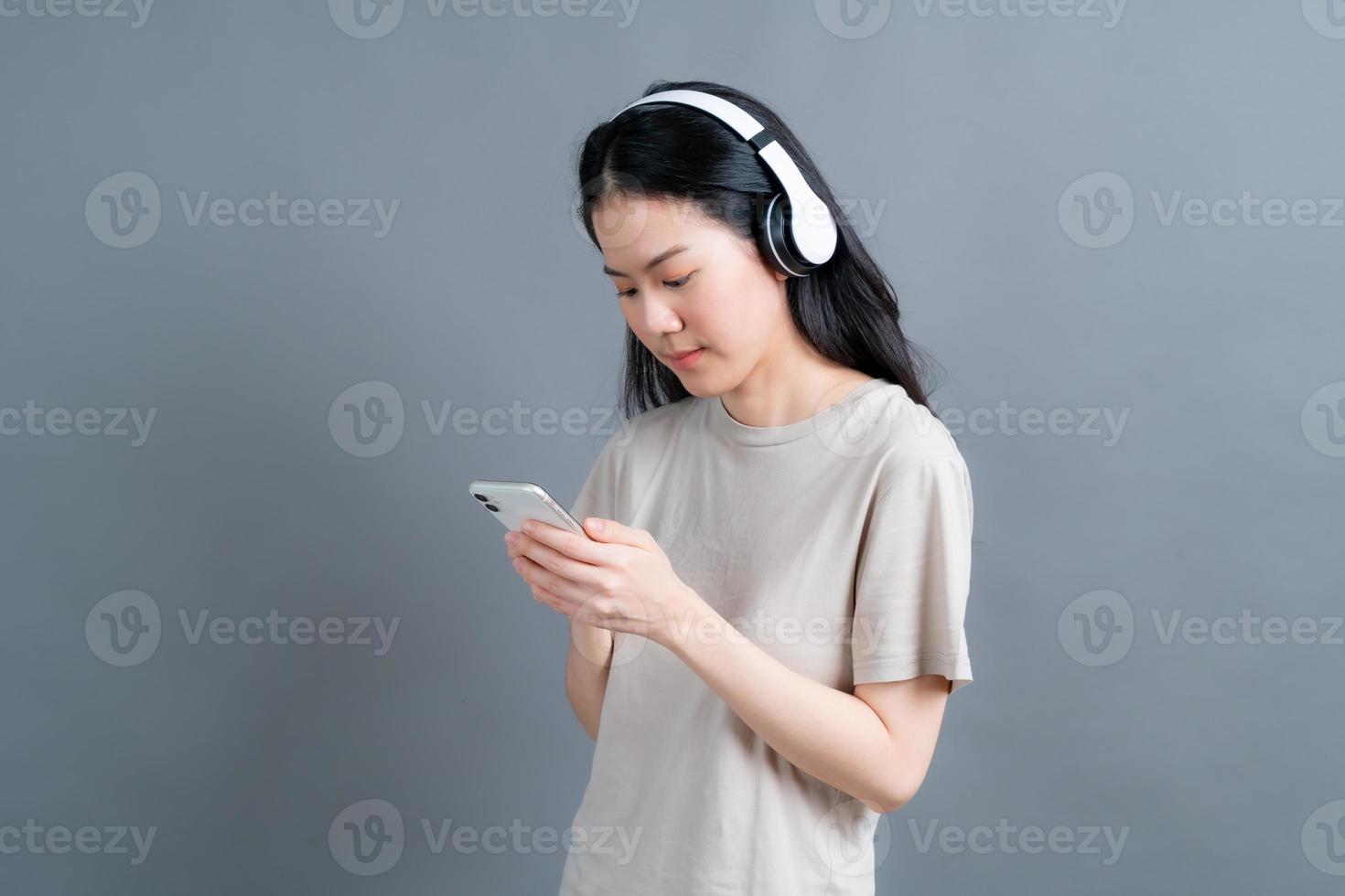 asiatisk kvinna bär trådlös hörlurar hålla smartphone tittar på telefonens skärm med mobilspelare app lyssnar online musik, lär sig främmande språk, tittar på video avkopplande på grå bakgrund foto