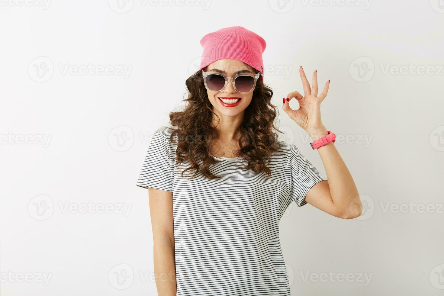 porträtt av ung Söt kvinna som visar Okej tecken, i rosa hatt, solglasögon, leende, isolerat foto
