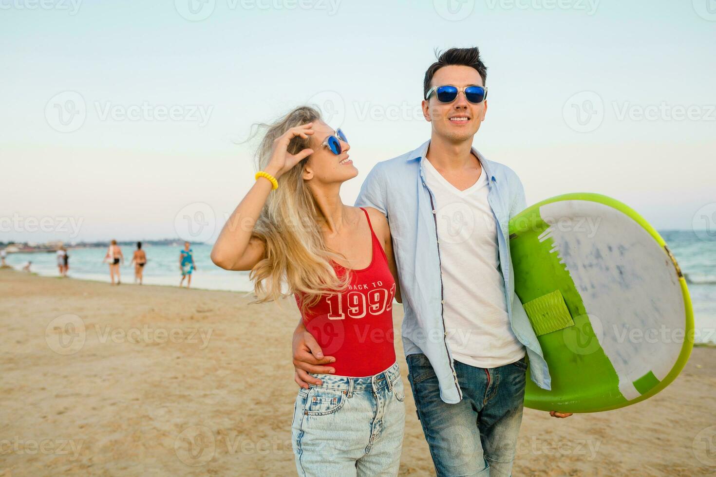 ung leende par har roligt på strand gående med surfa styrelse foto