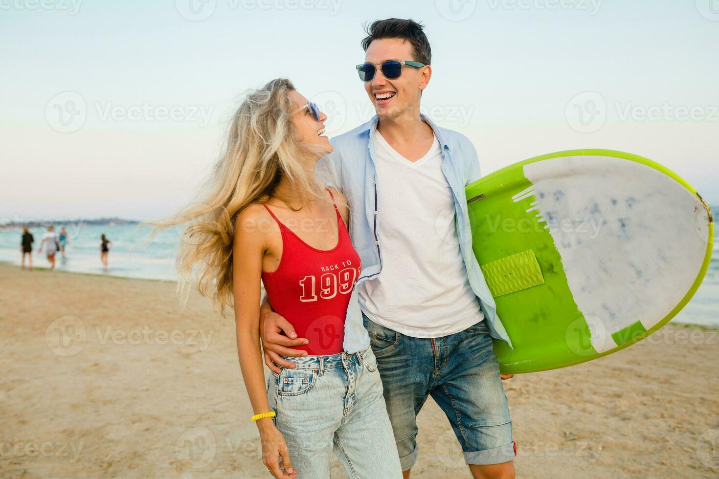 ung leende par har roligt på strand gående med surfa styrelse foto