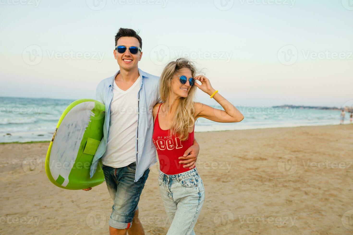 ung leende par har roligt på strand gående med surfa styrelse foto