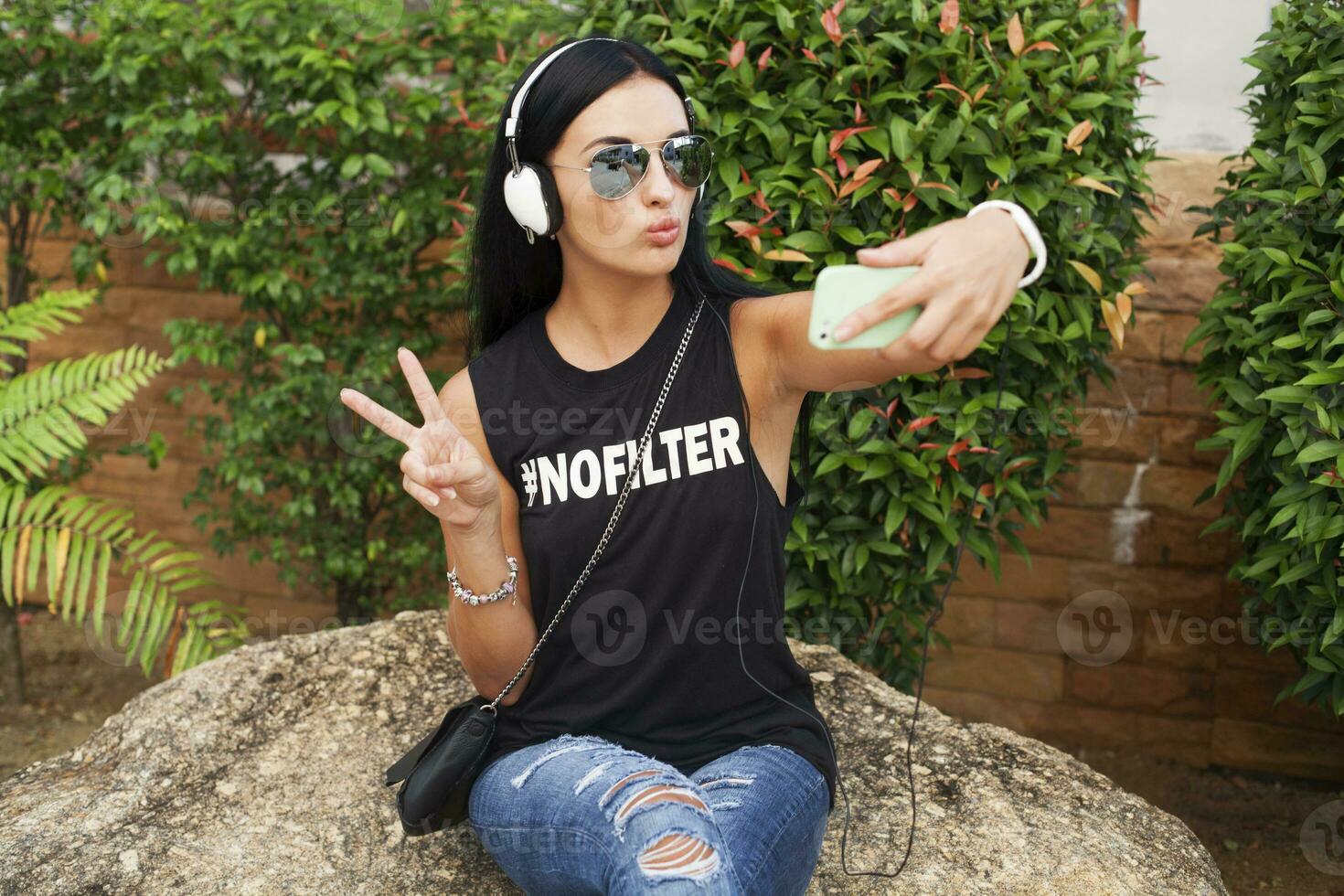 ung eleganta hipster kvinna i svart t-shirt, jeans, lyssnande till musik på hörlurar foto