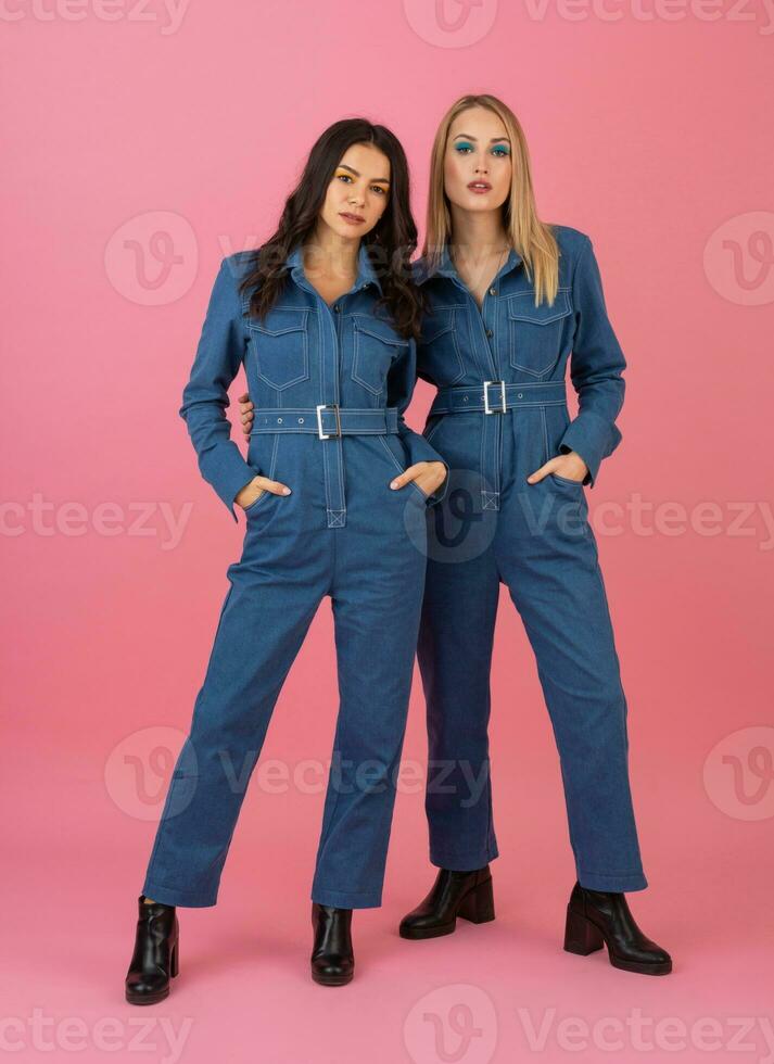 två upphetsad attraktiv flicka vänner aktiva kvinnor Framställ på rosa bakgrund i denim övergripande har roligt tillsammans mode trend foto