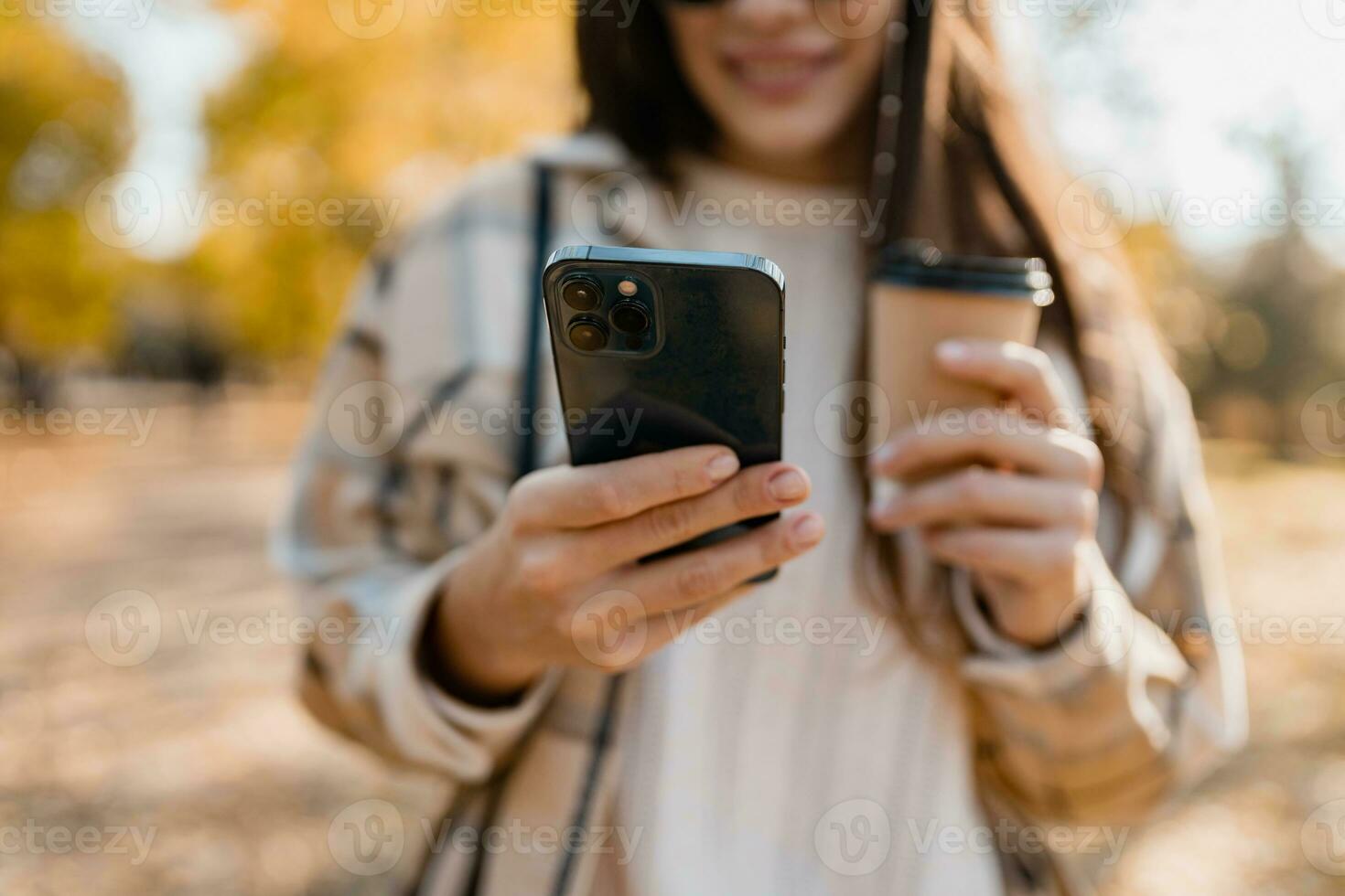 närbild händer innehav telefon av ung kvinna gående i höst parkera använder sig av app på smartphone foto