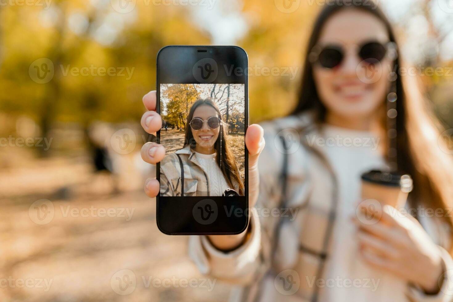 attraktiv ung kvinna gående i höst bär jacka använder sig av telefon foto