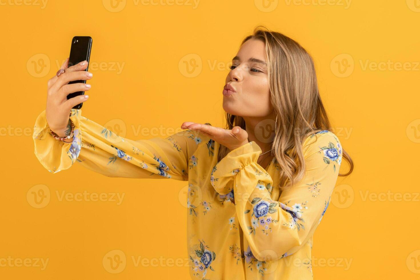 skön attraktiv leende kvinna i gul skjorta innehav smartphone foto