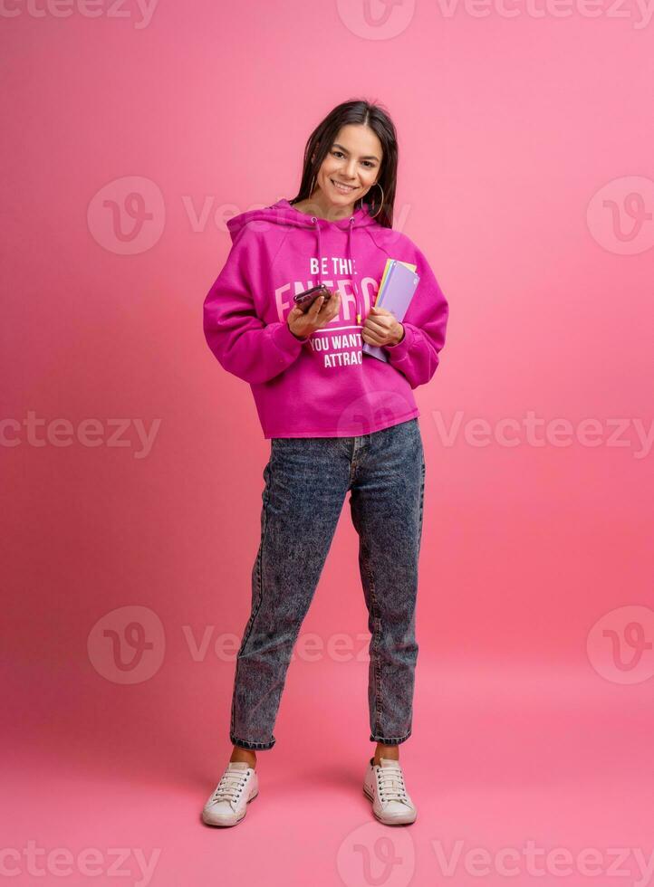 latinamerikan Söt kvinna i rosa luvtröja leende innehav innehav bärbara datorer och använder sig av smartphone foto
