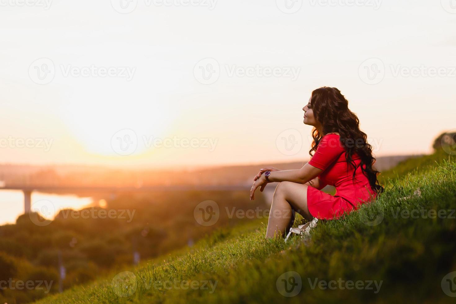 vacker ung flicka sitter i en sluttning täckt med grönt gräs foto