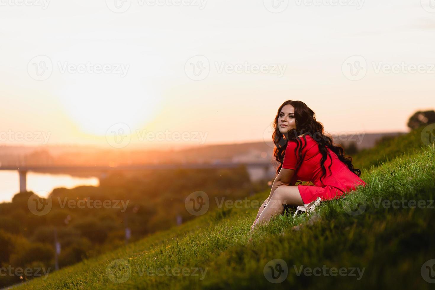 vacker ung flicka sitter i en sluttning täckt med grönt gräs foto