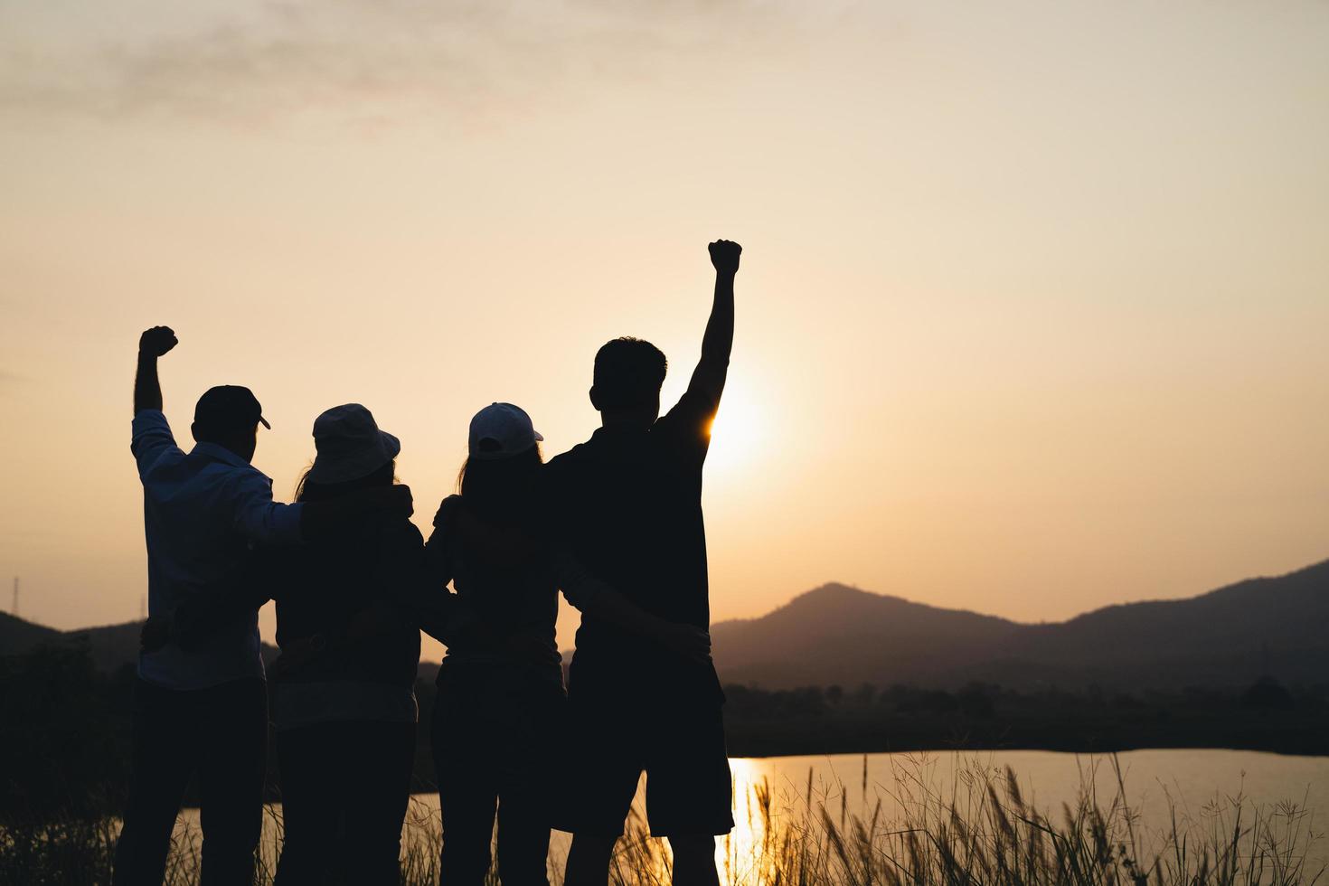 grupp människor med upphöjda armar tittar på soluppgången på berget bakgrunden. lycka, framgång, vänskap och samhällskoncept. foto