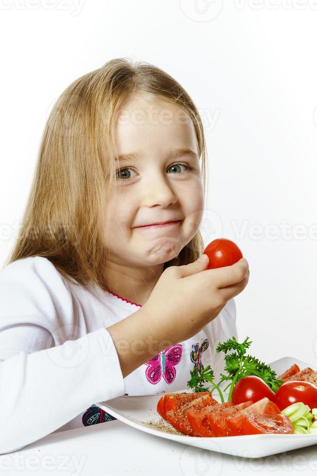 söt liten flicka med tallriken med färska grönsaker foto