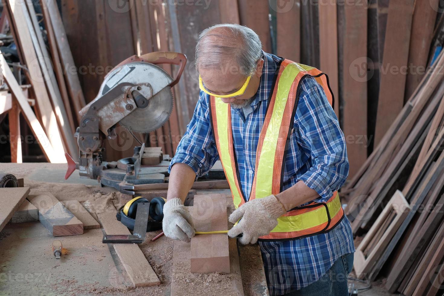 gammal asiatisk man snickare som arbetar i en träbearbetningsfabrik. de använder ett måttband och en penna och annan industriell utrustning som hammare, elektriska sågar och andra hantverktyg. foto