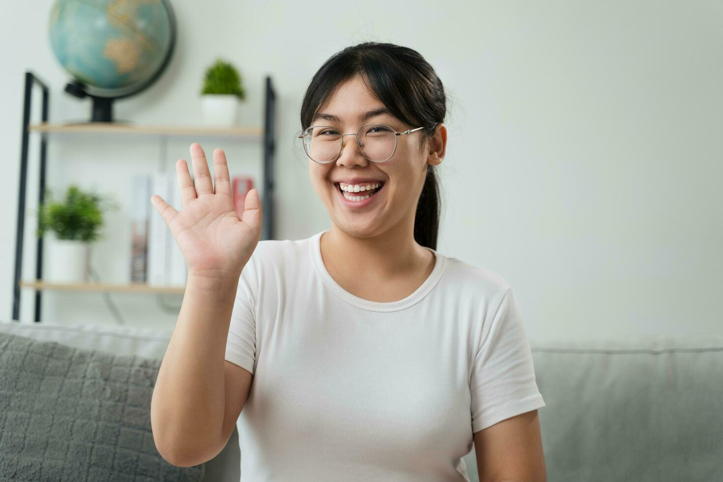 porträtt av ung asiatisk kvinna bär öga glasögon stor leende och ser på kamera med känsla Lycklig och positiv i levande rum på Hem, möte, video konferens. foto