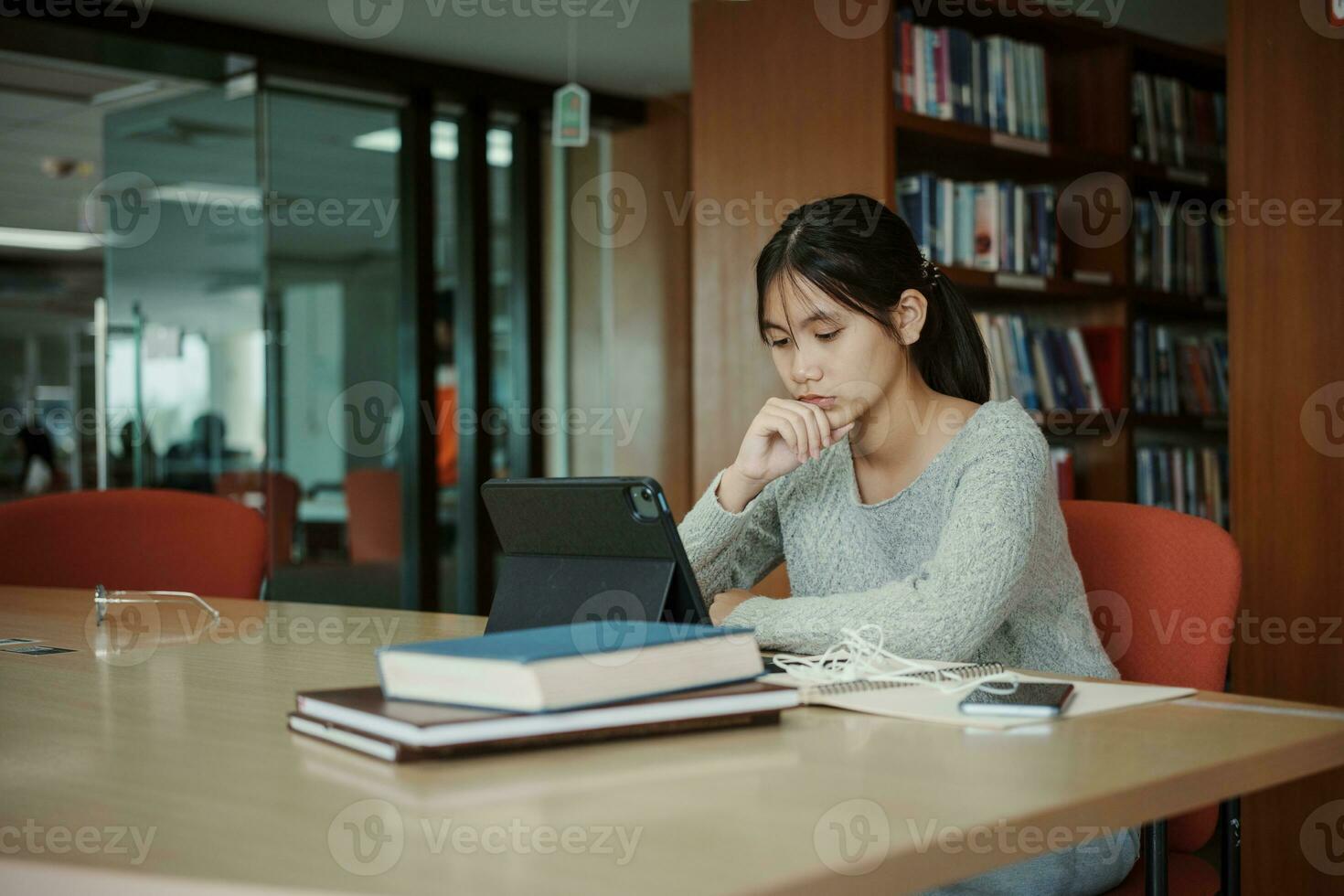 asiatisk studerande kvinna läsa böcker i bibliotek på universitet. ung flicka påfrestning trött ha problem medan studie hård. sorg begrepp foto