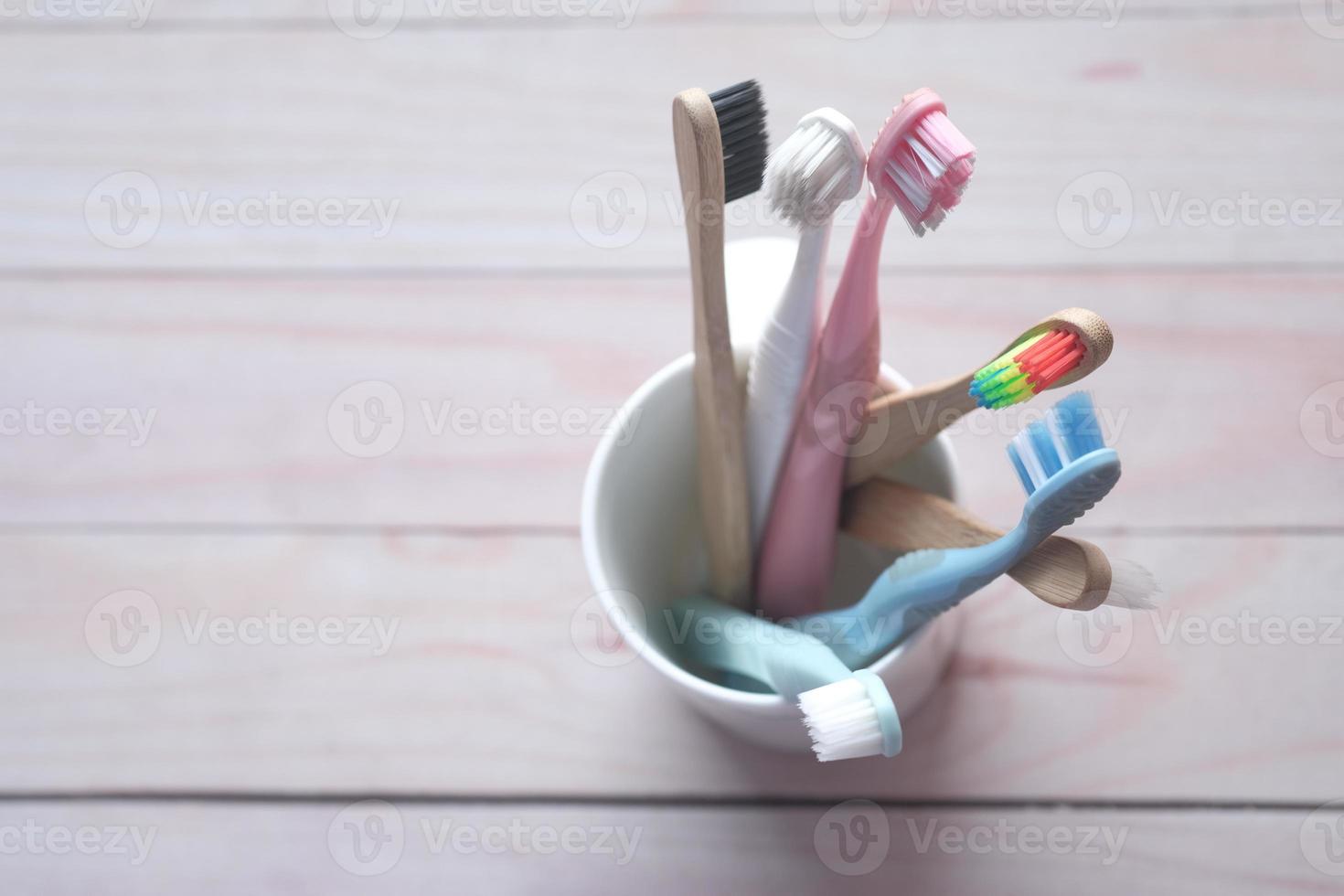 färgglada tandborstar i vit mugg mot en vägg foto