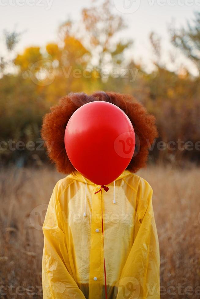 kvinna i en gul regnrock som håller en röd ballong på bakgrunden av skogen. foto