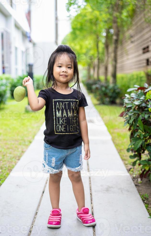 liten flicka med en mango i handen foto