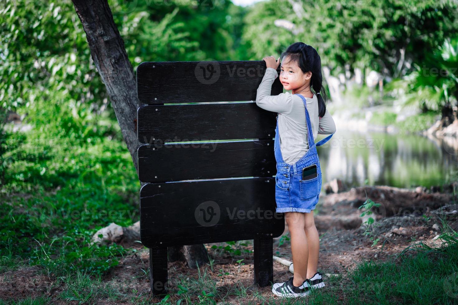 liten asiatisk tjej lade mobiltelefonen i fickan med träetikett foto