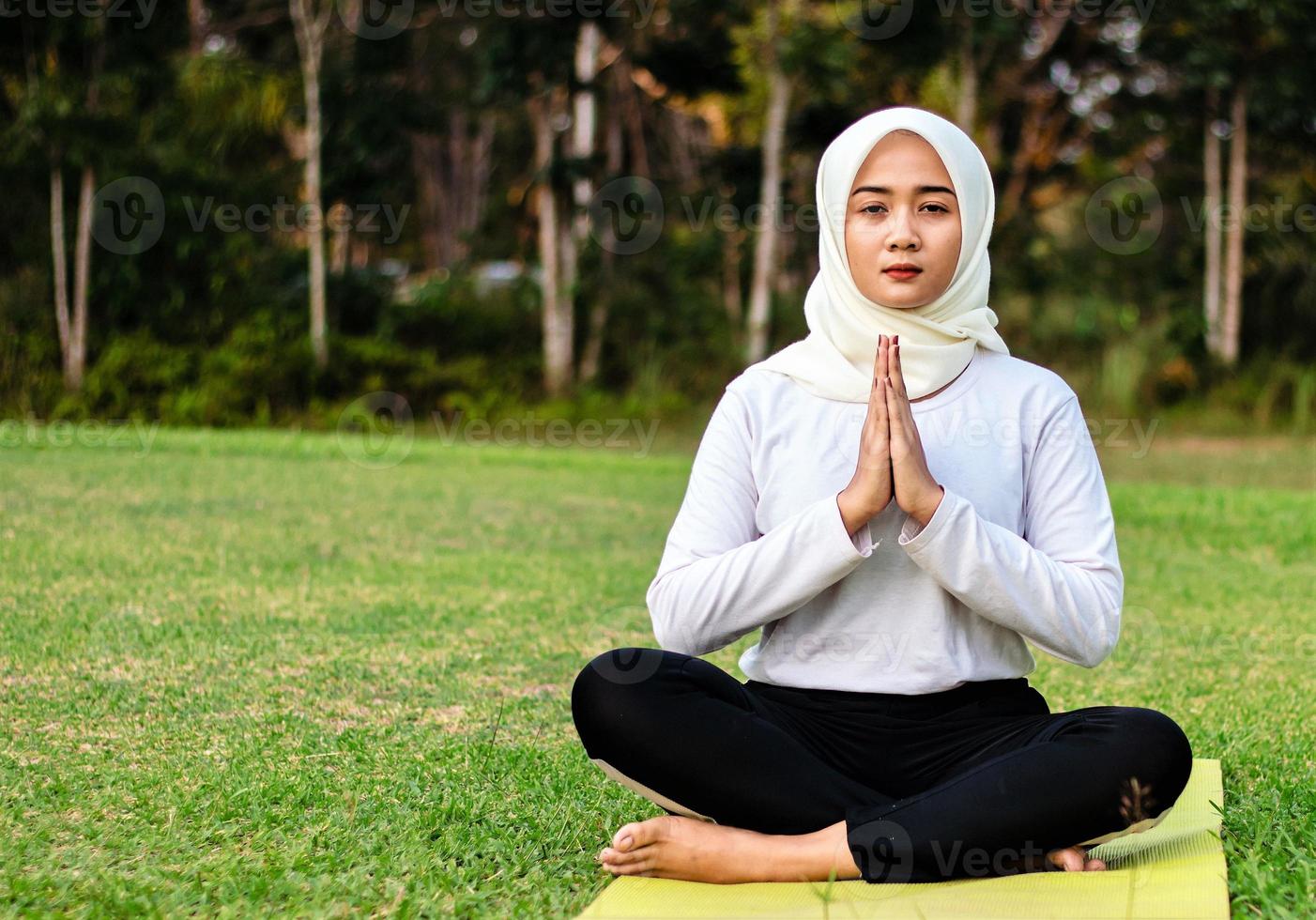 ung asiatisk muslimsk kvinna som sitter på gräset och njuter av meditation foto