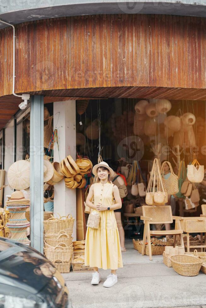 ung asiatisk kvinna resande i klänning med hatt reser till korg- affär på chang moi kao väg, turist besök på de gammal stad i chang maj, thailand. Asien resa, semester och sommar Semester begrepp foto