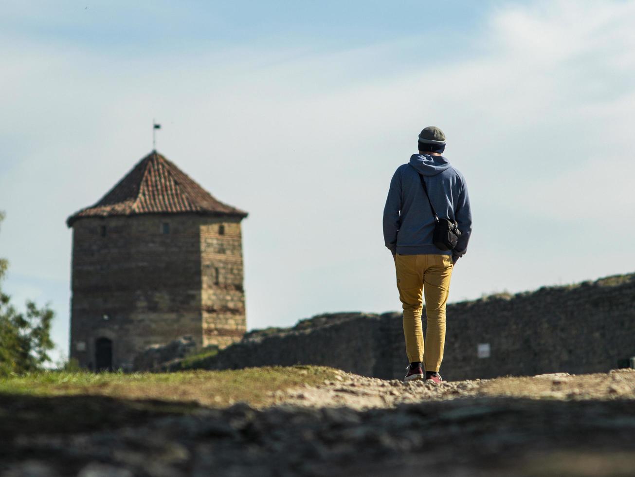 en man i hujtröja och stickad hatt går längs vägen till fästningen mot bakgrund av tornet och den blå himlen foto