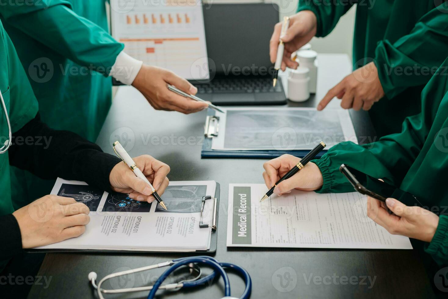 medicinsk team har en möte med doktorer i vit labb rockar och kirurgisk scrubs sittande på en tabell diskuterar en patienter arbetssätt uppkopplad använder sig av datorer i de medicinsk foto