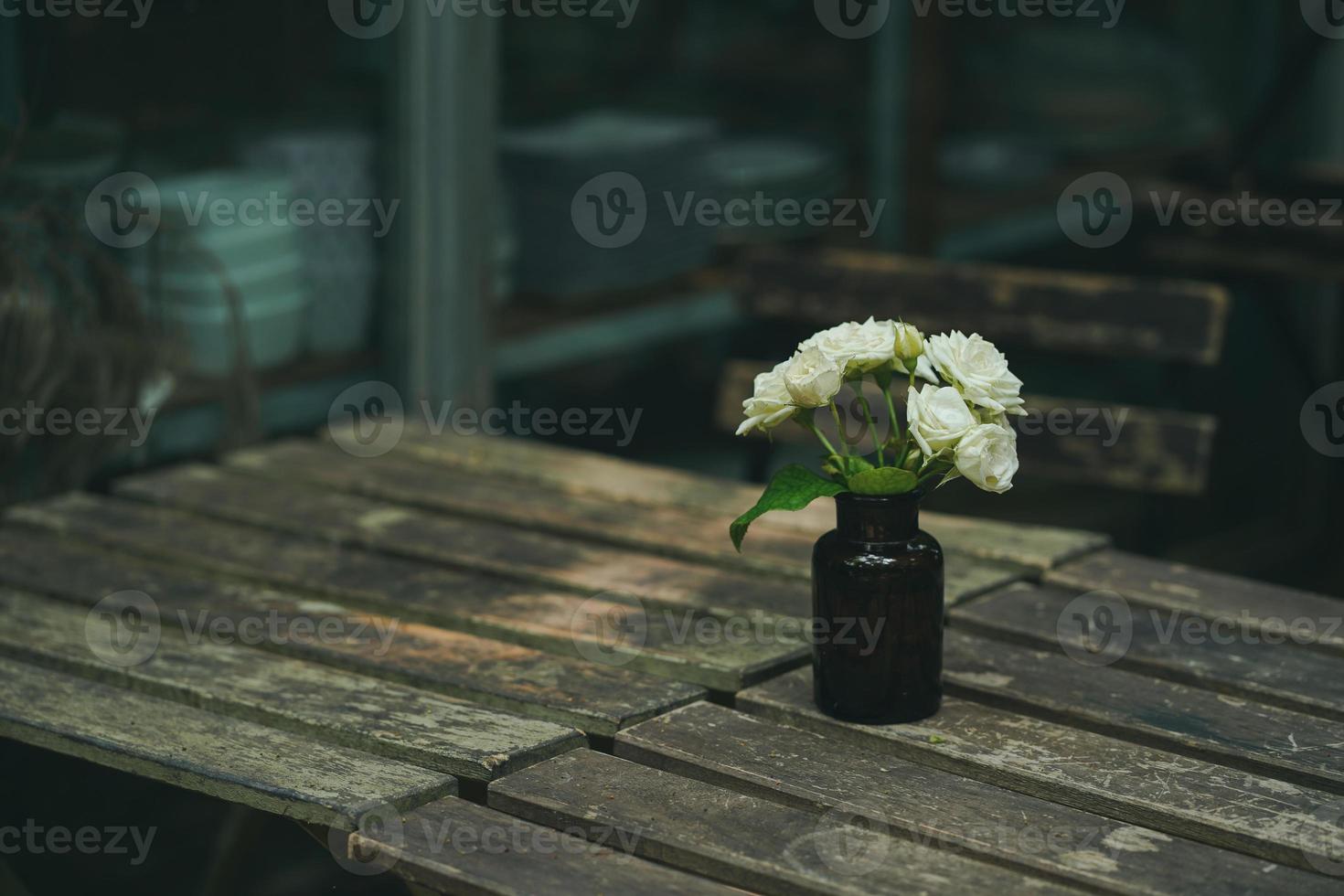 vackra blommor i en brun glasflaska placerad på ett träbord i trädgården på morgonen foto