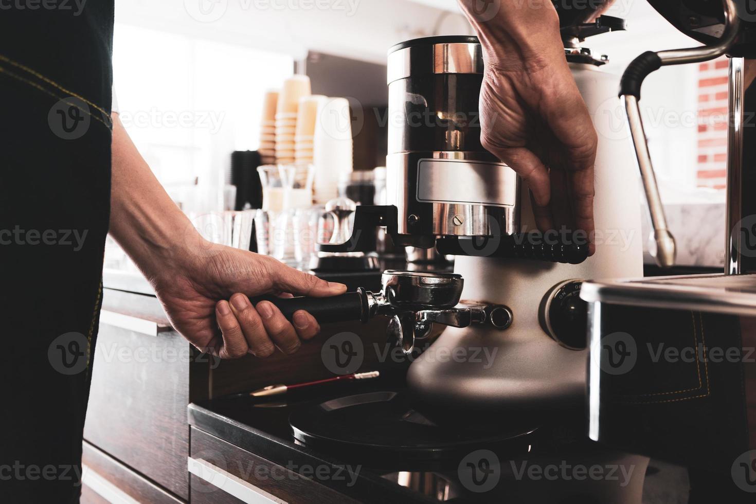 ung asiatisk man som använder kaffekvarnmaskinen för att stryka kaffebönor på kaféet. barista koncept foto