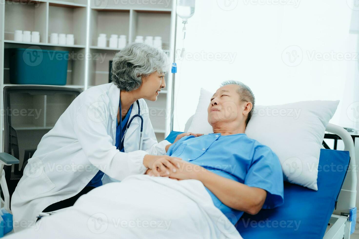 asiatisk läkare i vit kostym ta anteckningar medan diskuterar och asiatisk äldre, man patient vem liggande på säng med tar emot salin lösning i sjukhus eller klinik. foto