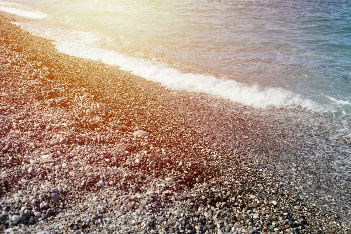 Bank av småsten med de hav och strand i de bakgrund foto