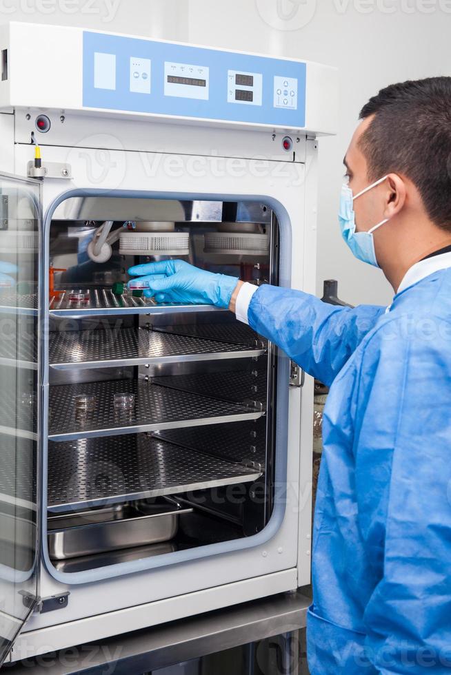 ung laboratorieforskare som introducerar en petriskål i en inkubator foto