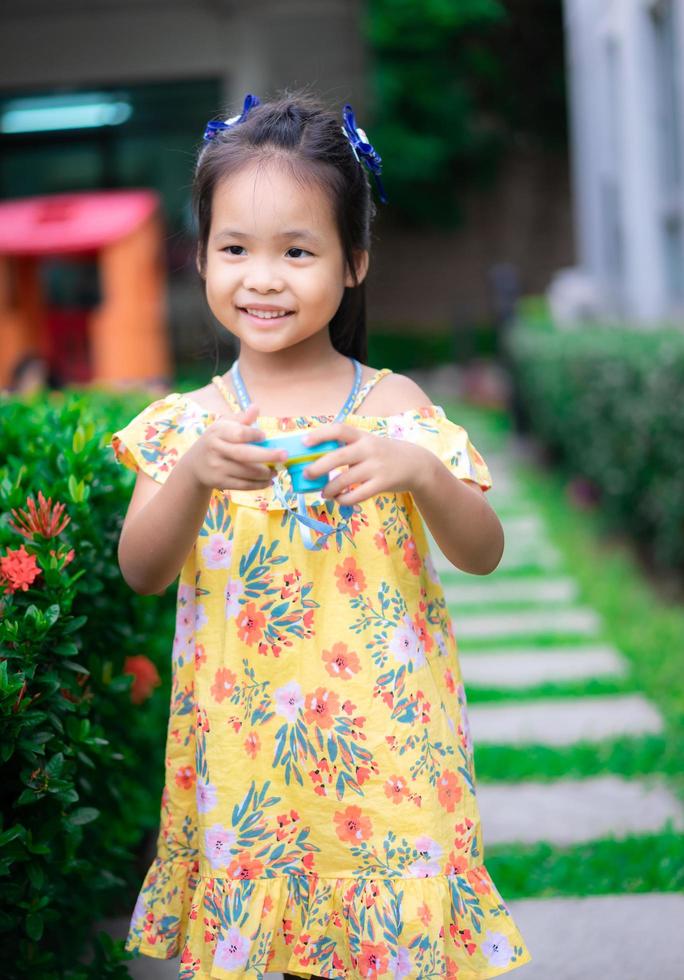 porträtt av söt liten asiatisk tjej ha kul med leksakskamera i parken foto