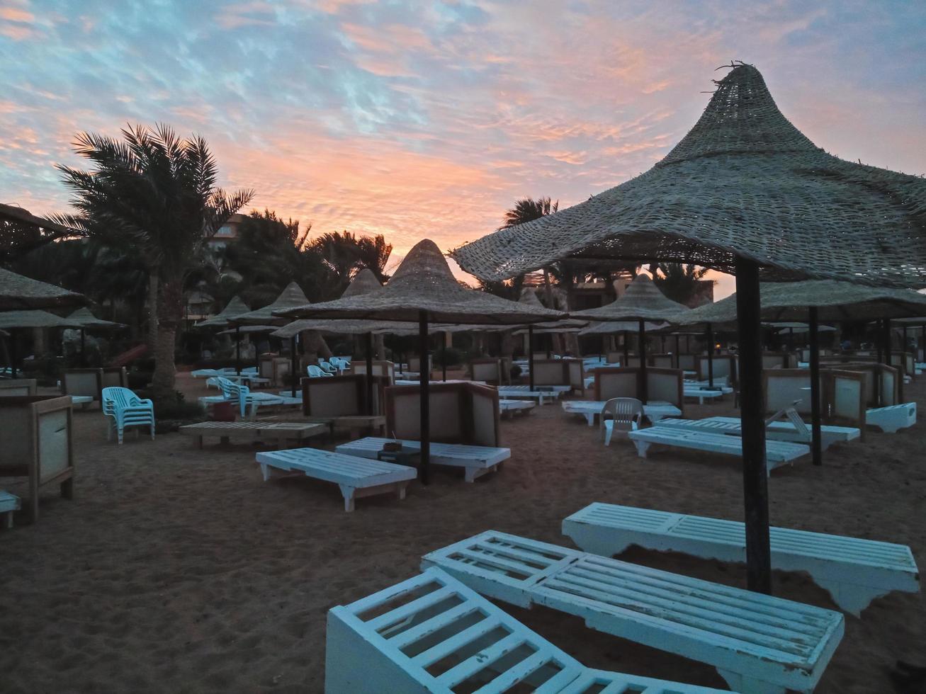 solstolar och halmparaplyer och vacker solnedgång på stranden i Hurghada, Egypten foto