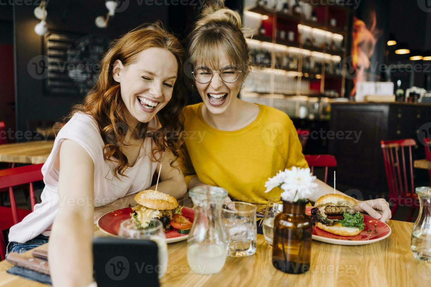 två Lycklig kvinna vänner har burger och tar en selfie i en restaurang foto