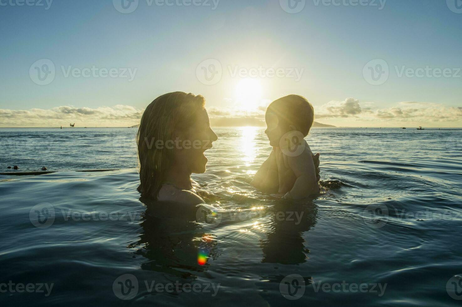 franska polynesien, tahiti, papeete, kvinna spelar med henne liten bebis i ett oändlighet slå samman på solnedgång foto