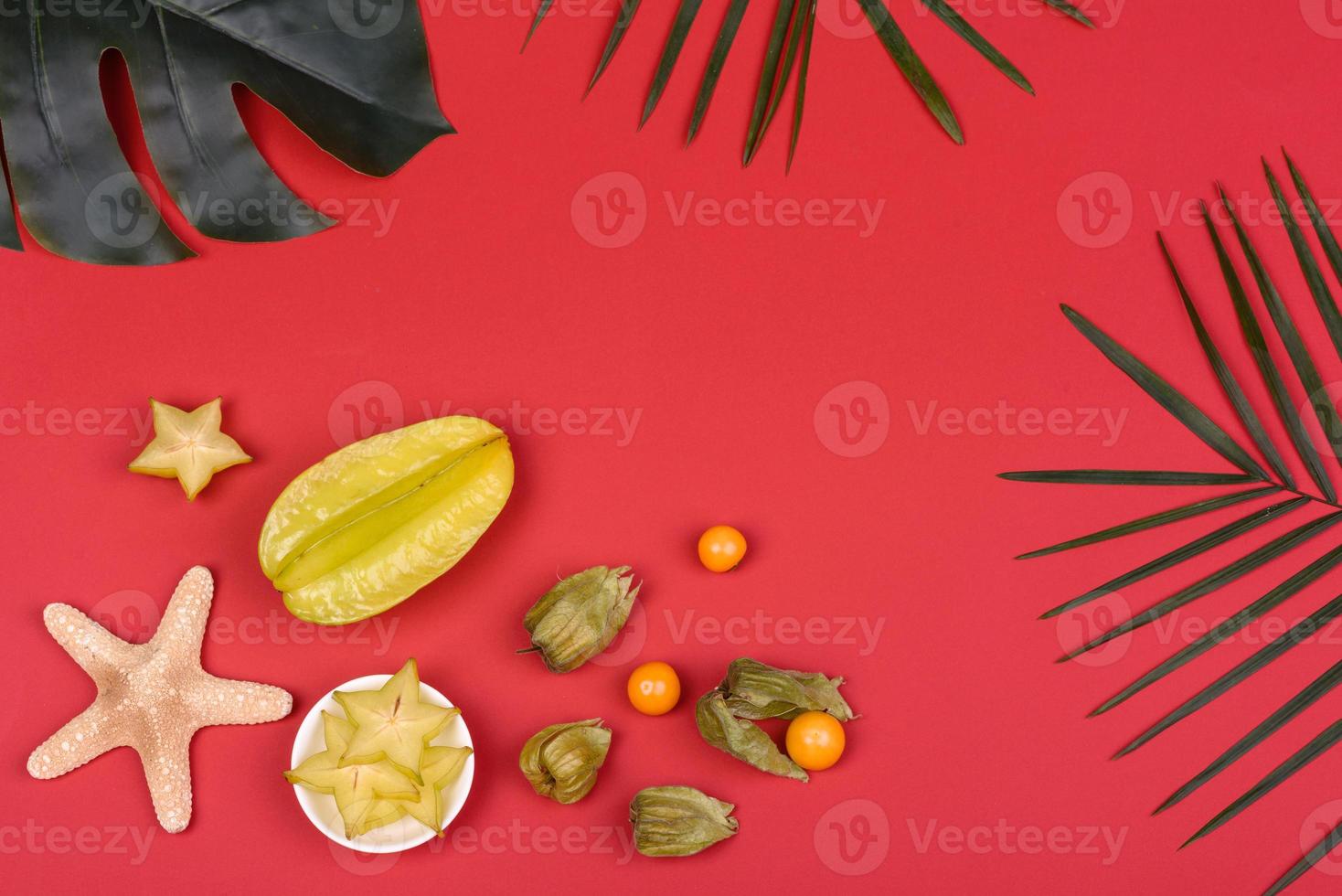 fruktkarambol, strandtillbehör och bladverk av en tropisk växt på färgat papper foto