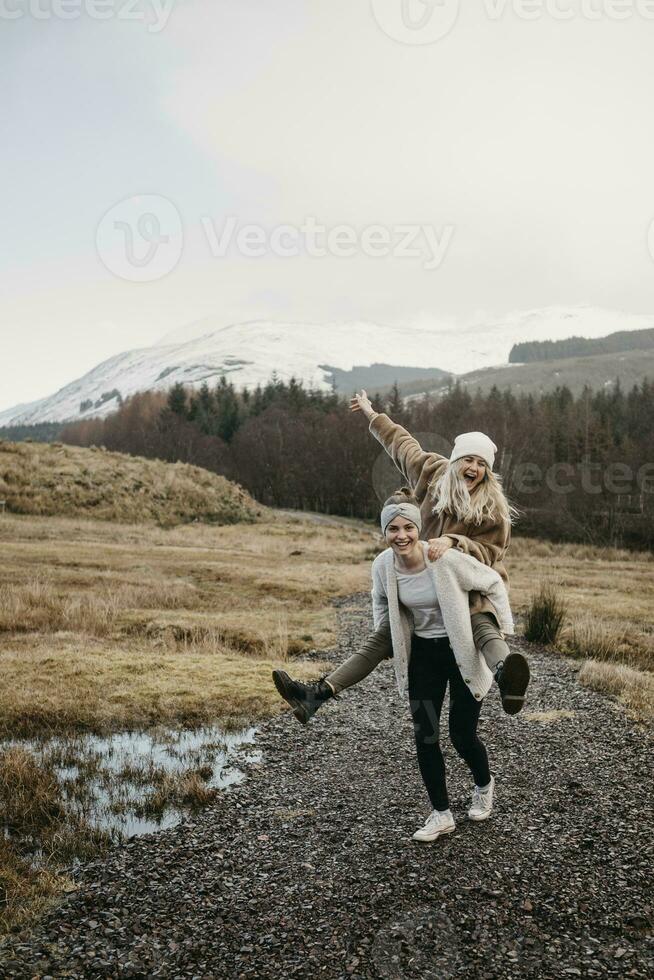 Storbritannien, Skottland, Lycklig ung kvinna bärande vän piggyback i lantlig landskap foto