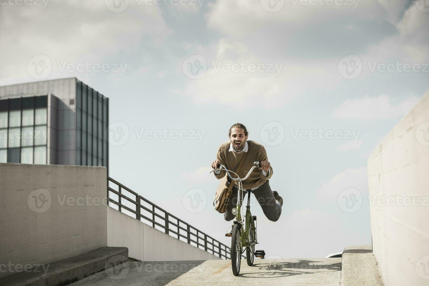 skrattande affärsman ridning ner en ramp på hans cykel foto