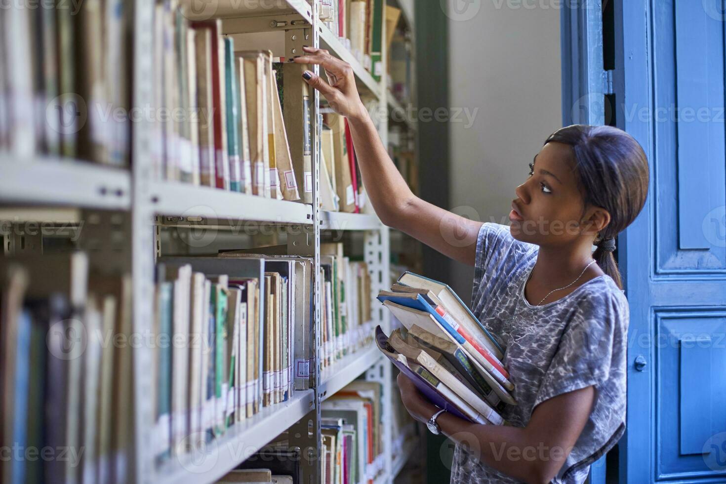 ung kvinna kontroll de böcker på de bokhyllor på nationell bibliotek, maputo, mocambique foto
