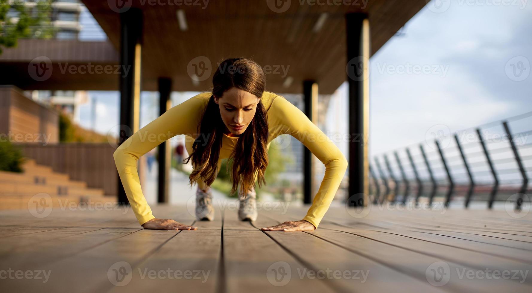 ung kvinna utför pushups på trä gångväg vid floden foto