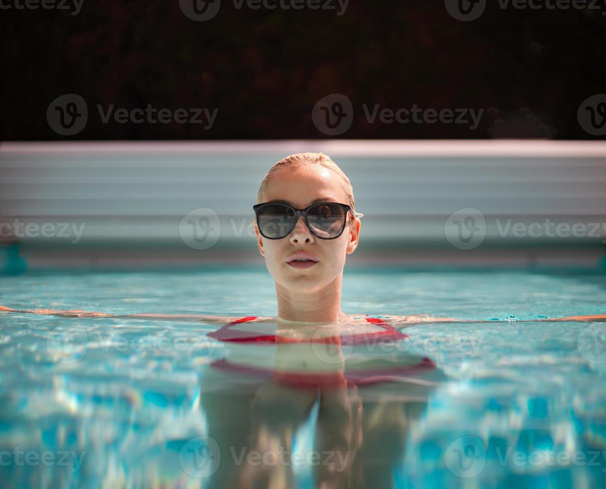 ung vacker sexig tjej njuter av att simma i den privata poolen och koppla av i solen foto