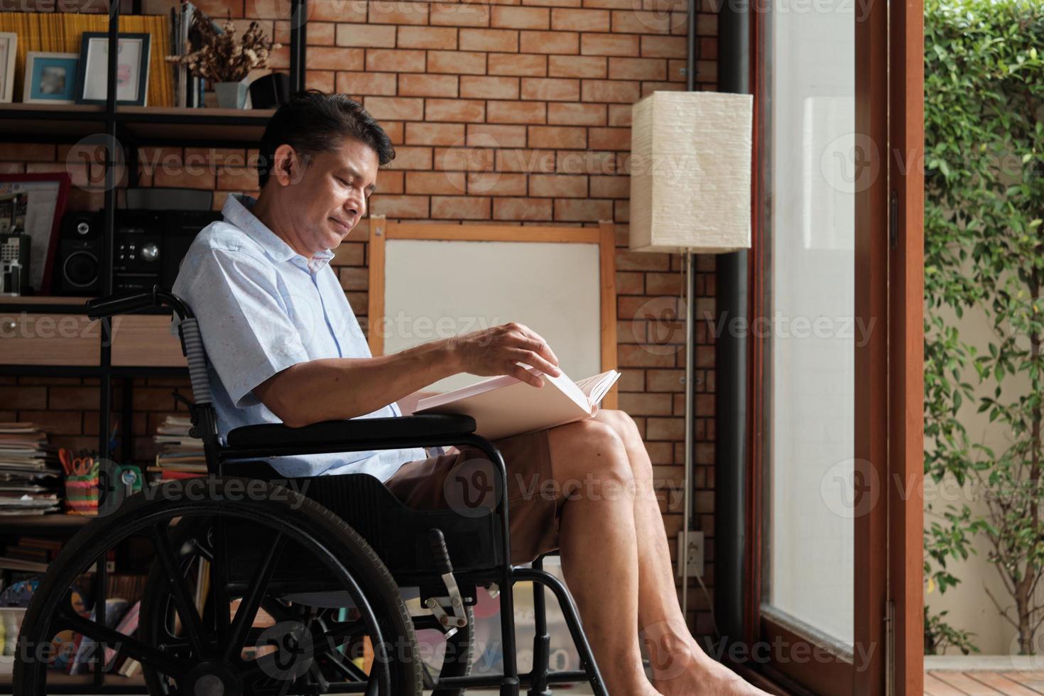 pensionerad man läser en bok i rullstol hemma. foto