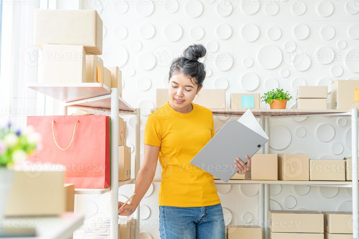 ung asiatisk kvinna som kontrollerar varor på lagerhylla på lager - online-försäljning eller shopping online-koncept foto